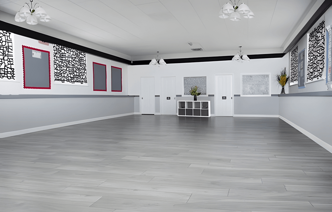 Spacious, empty hall with light grey wooden flooring, white walls, modern abstract art, ceiling lights, and a cabinet with vases of flowers.
